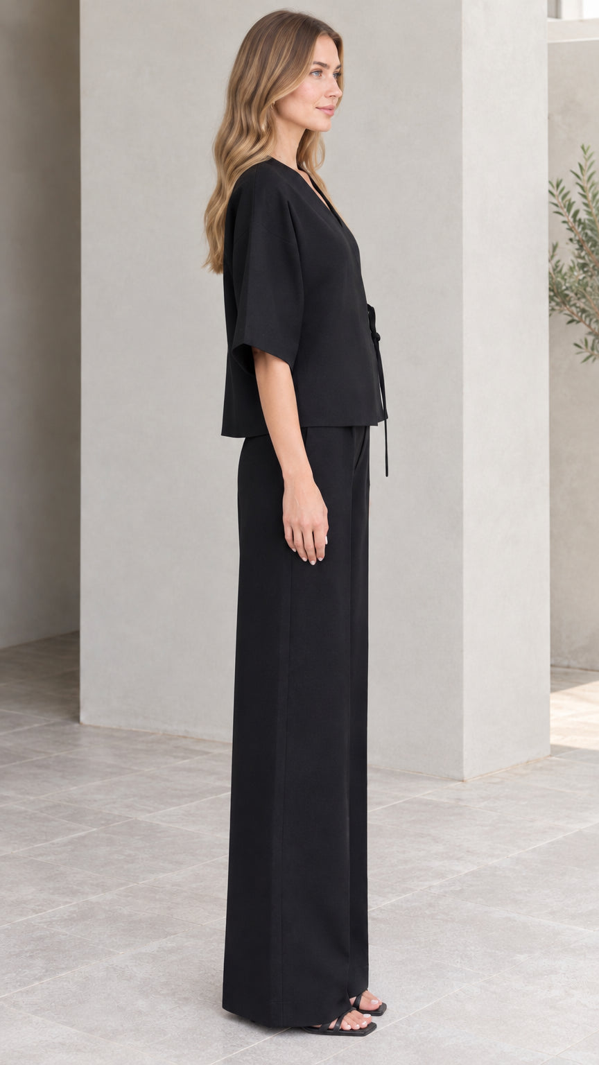Side full-length profile of model in black two-piece wrap pants suit