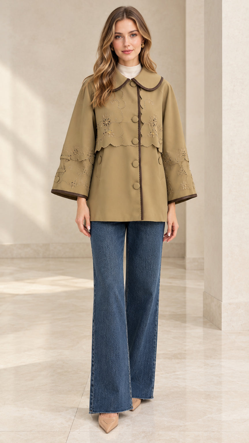 Front full-length view of woman wearing khaki embroidered capelet jacket with wide-leg jeans