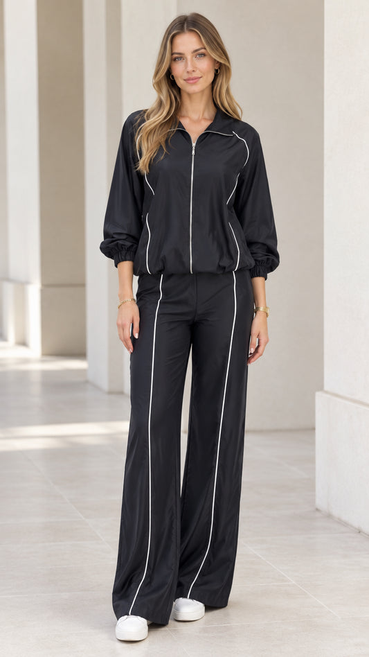 Front full view of woman wearing black tracksuit set with contrast white piping and wide leg pants
