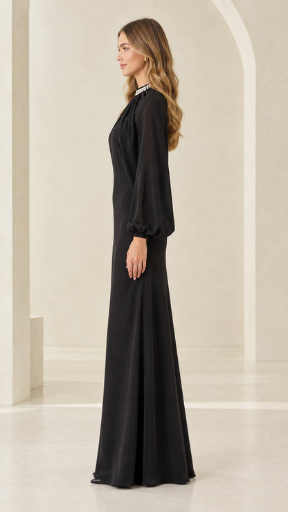 Side profile view of woman modeling black long sleeve cape formal gown