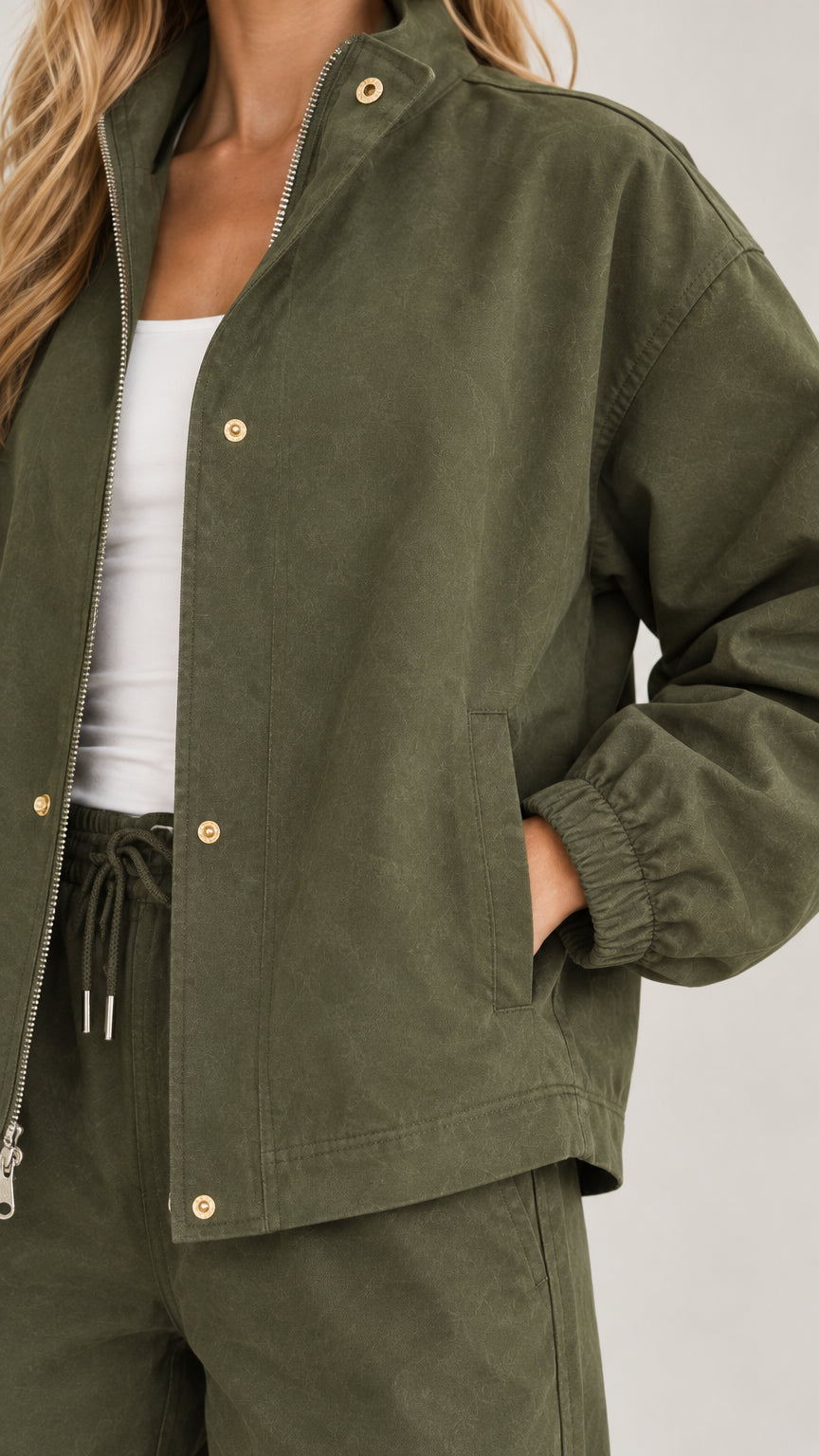 Close-up detail of olive green jacket zipper, snap buttons, and drawstring waist
