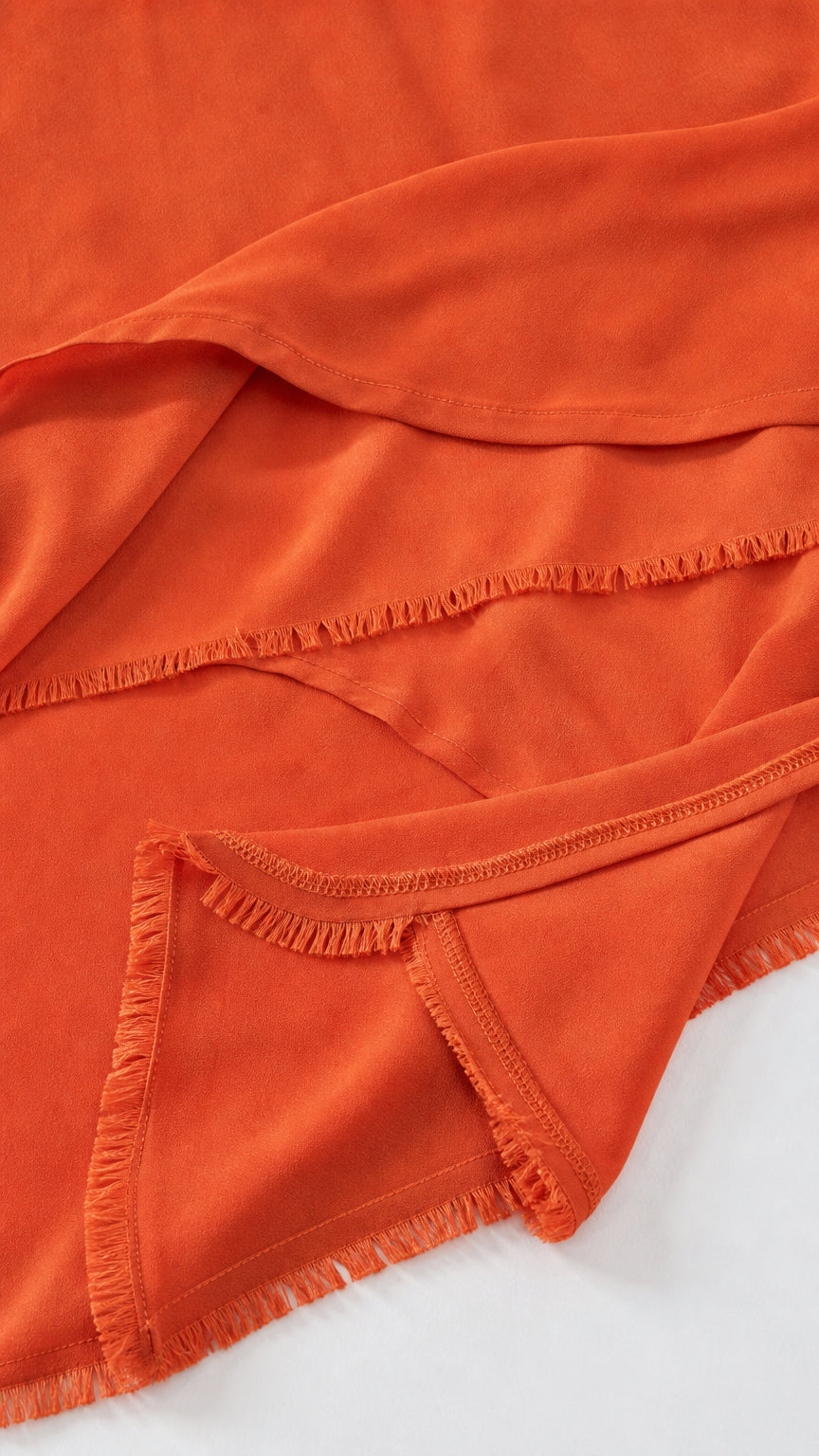 Close-up detail of rust orange fabric and frayed ruffle hem