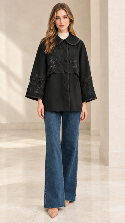 Full-length front view of woman wearing black embroidered scalloped capelet jacket
